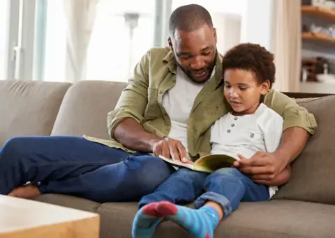 Father reads book to son on couch.