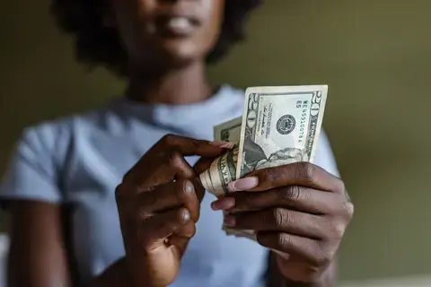 Woman in blue shirt holding twenty dollar bills with green background.