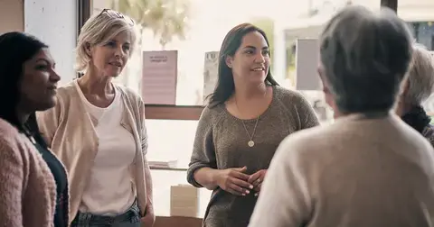 A group of women of various ages and backgrounds standing in a circle conversing.