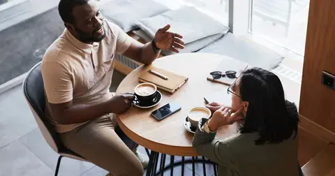 Man and woman sit at small table drinking coffee discussing the women&#39;s wage gap as it relates to retirement planning.